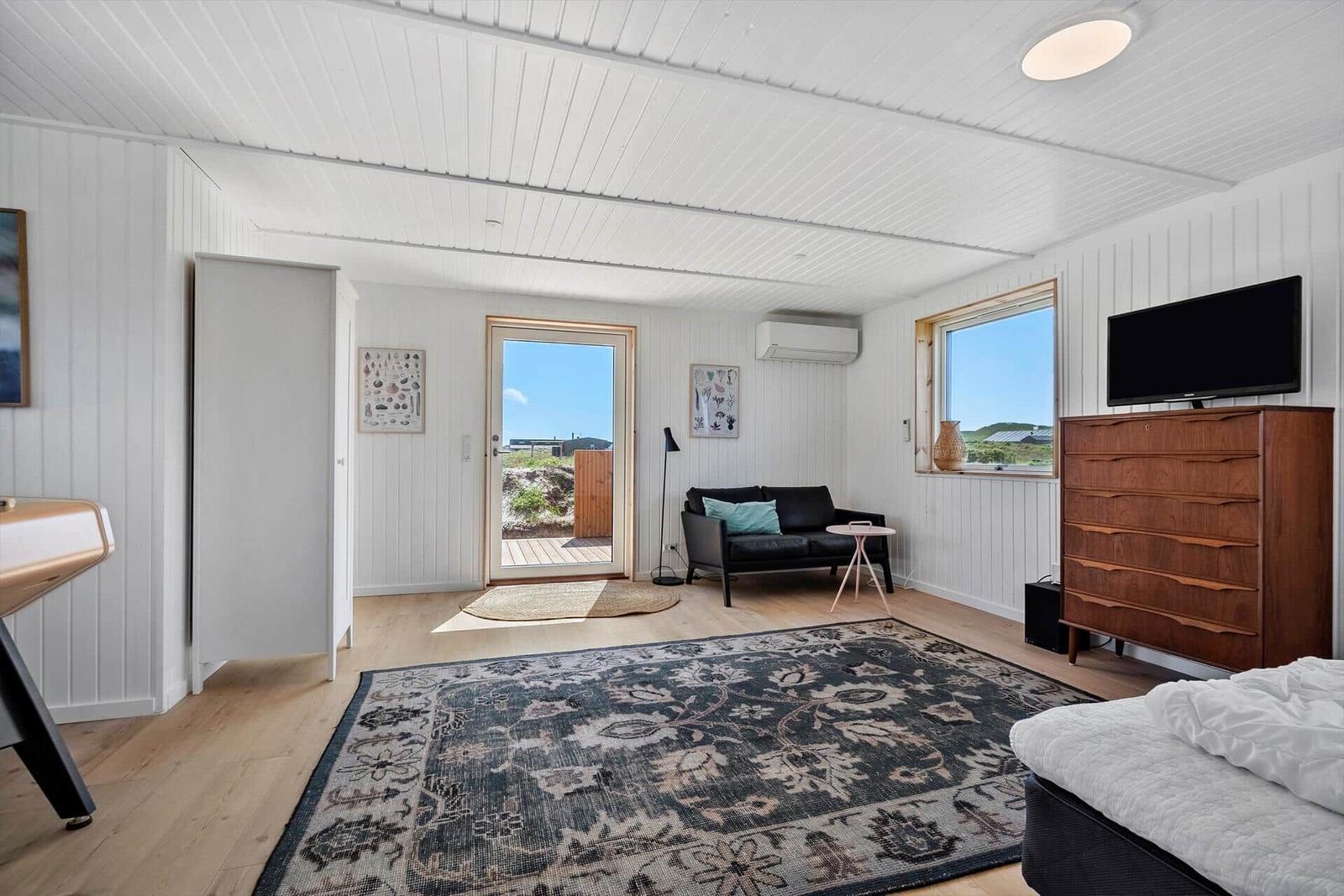 Schlafzimmer mit Bett, TV-Schrank und Sitzgelegenheit. Durchgang zur Terrasse mit Blick.