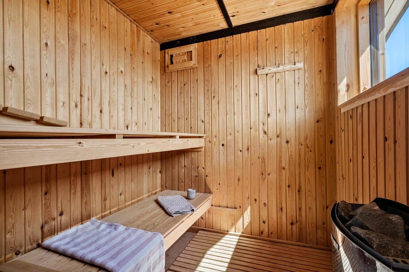 Holzsauna mit Bänken, Handtuch und Steinofen.