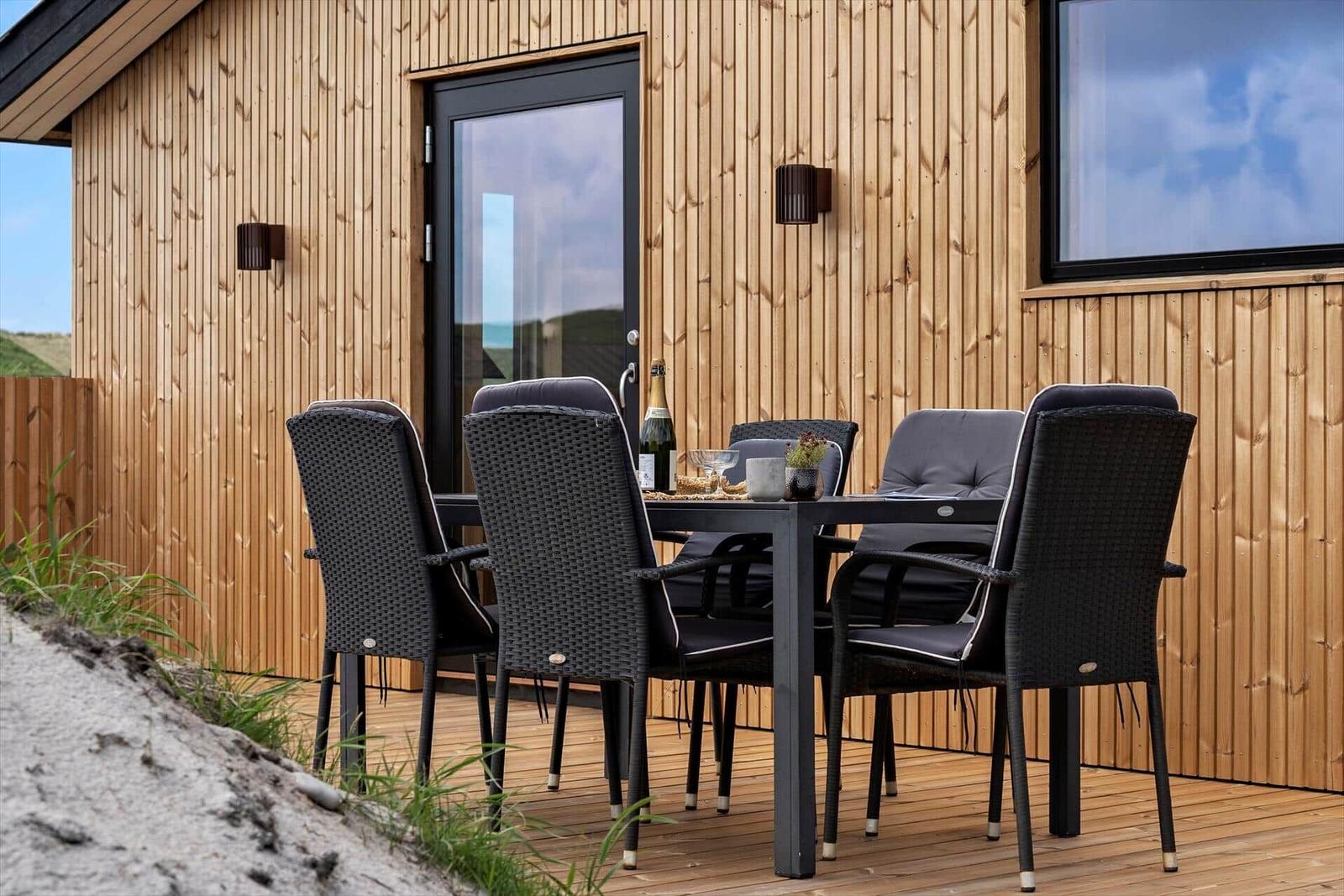 Terrasse mit Tisch und Stühlen vor Holzhäusern mit Fenstern.