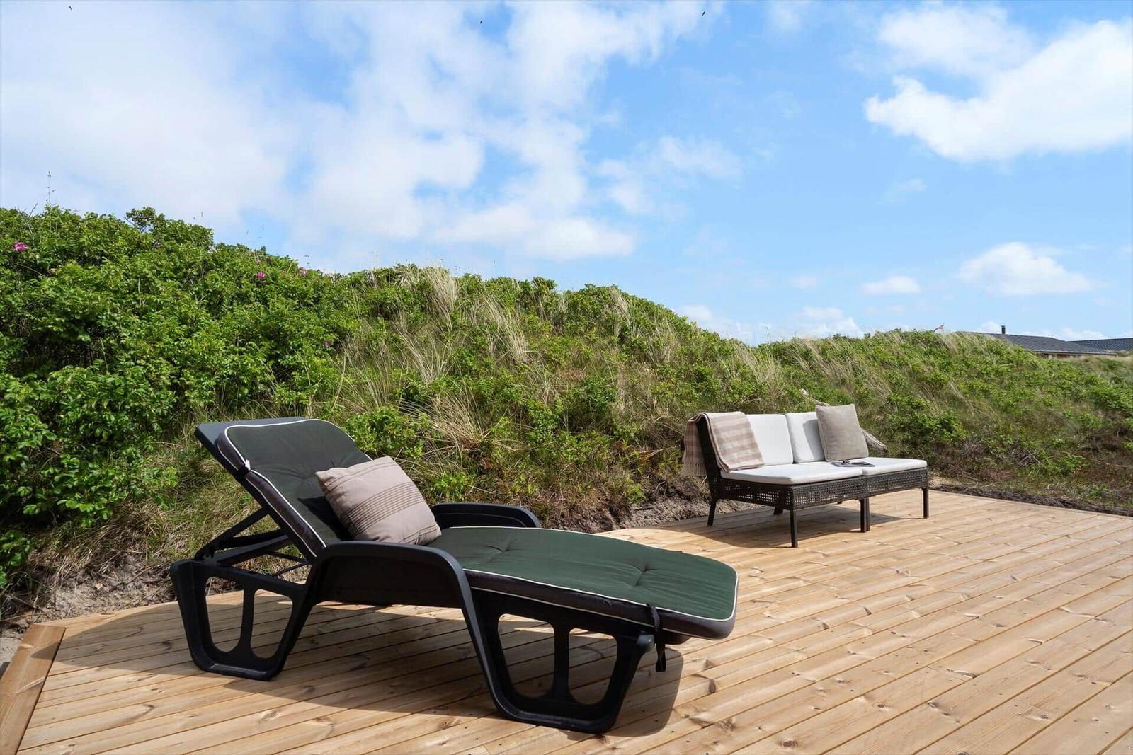Terrasse mit Liege und Sofa vor grüner Dünenlandschaft.