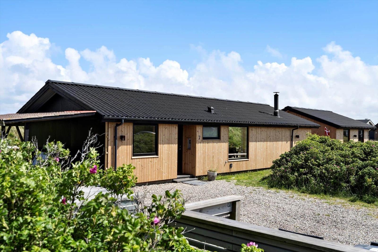 Moderne Holzhütte mit schwarzem Dach und Garten. Einbauküche und Schlafzimmer.