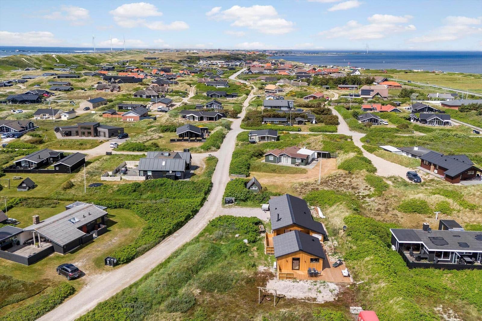 Aerial view of vacation homes on grassy dunes near the sea.
