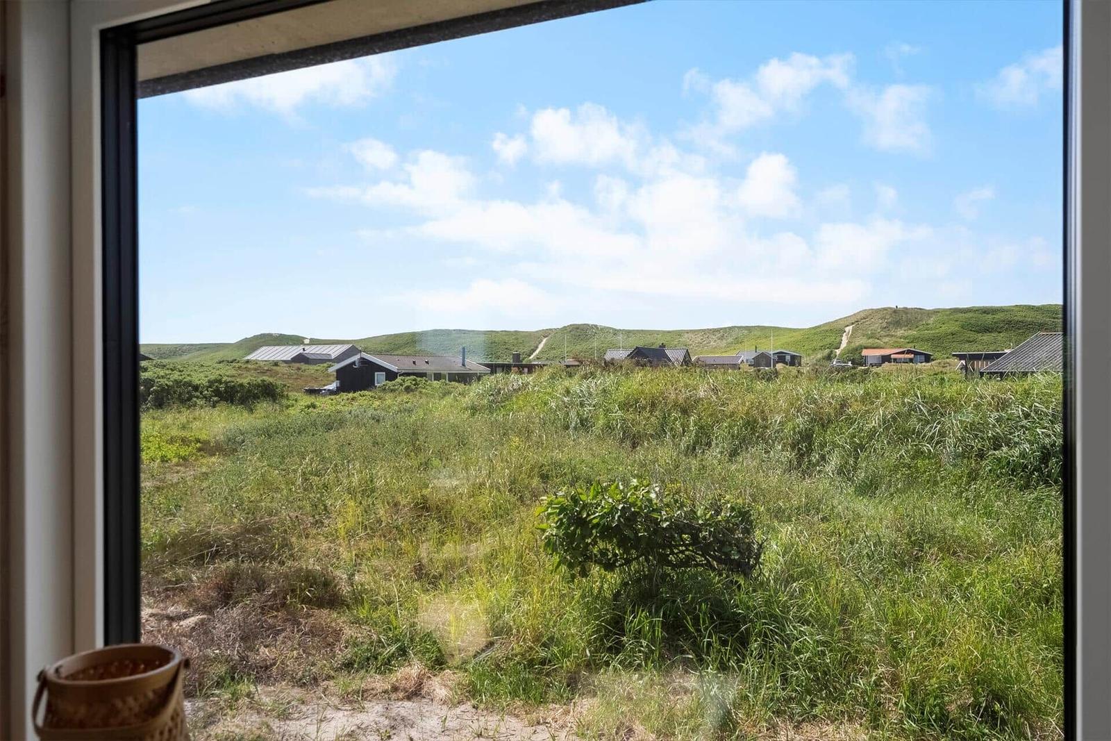 Durch das Fenster sieht man Grasland und Häuser im Hintergrund unter blauem Himmel.