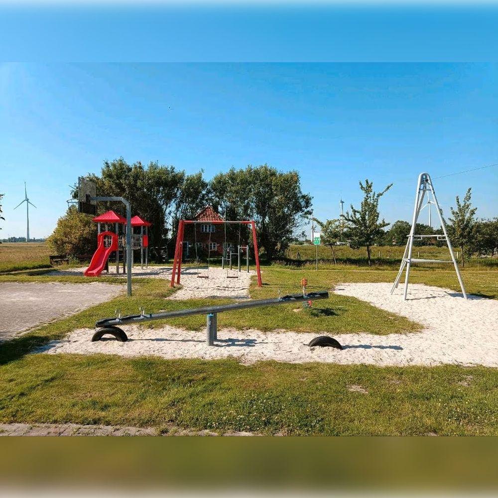 Kinderfreier Spielplatz mit Rutsche, Schaukel und Klettergerüst auf Sandfläche.