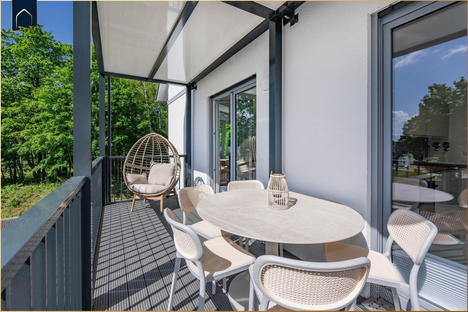 Terrasse mit Esstisch, Stühlen und Hängesessel. Blick in den Wald.