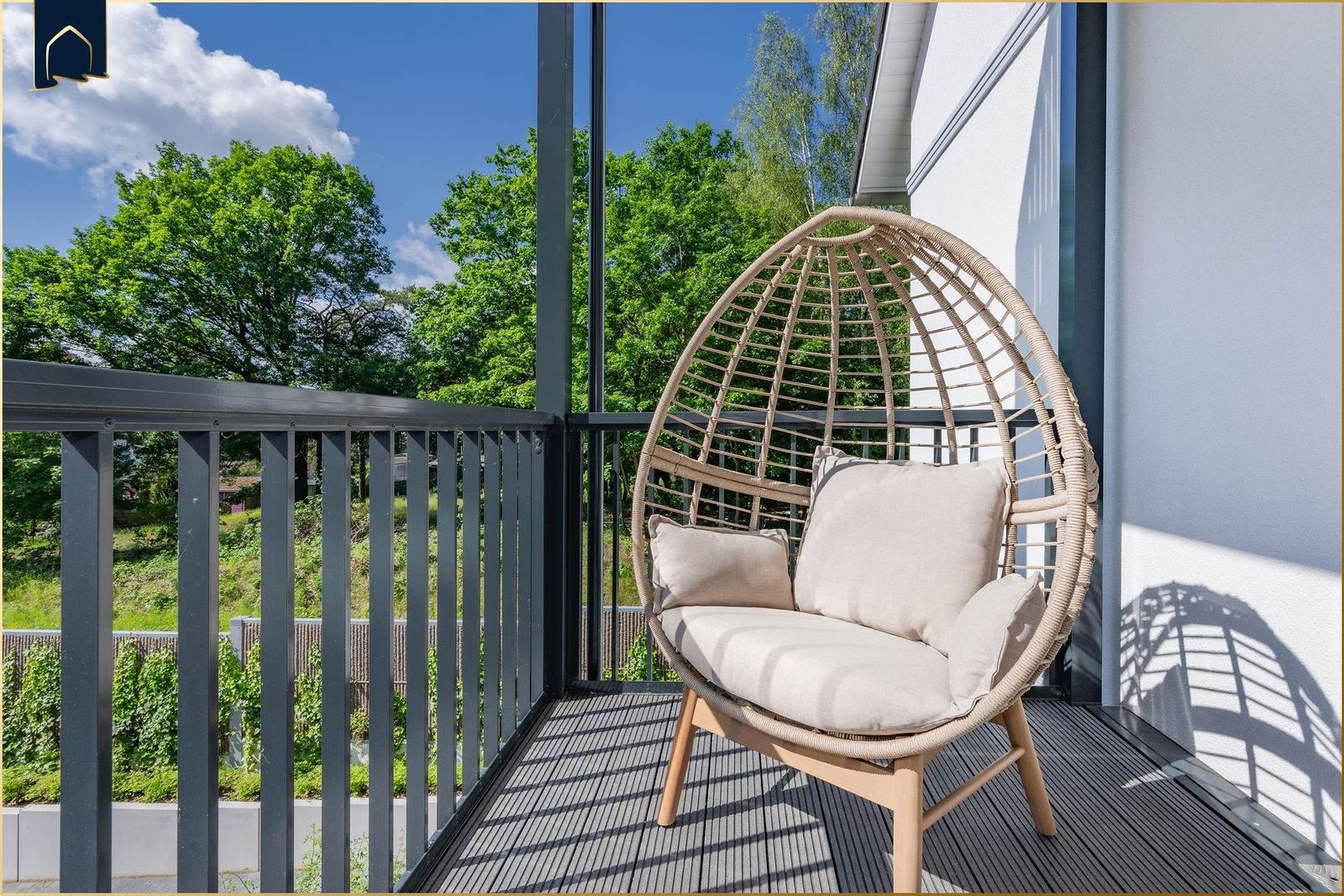 Terrasse mit Rattan-Sessel und Blick auf grüne Bäume.
