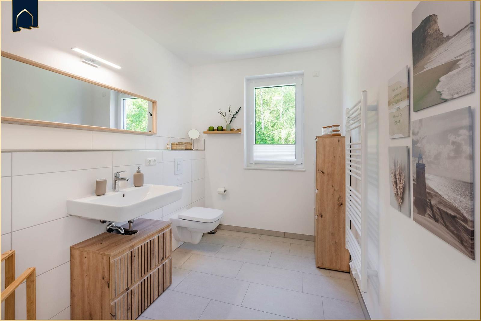 Badezimmer mit Waschbecken, Toilette und Fenster. Holzregale und Wandbilder.