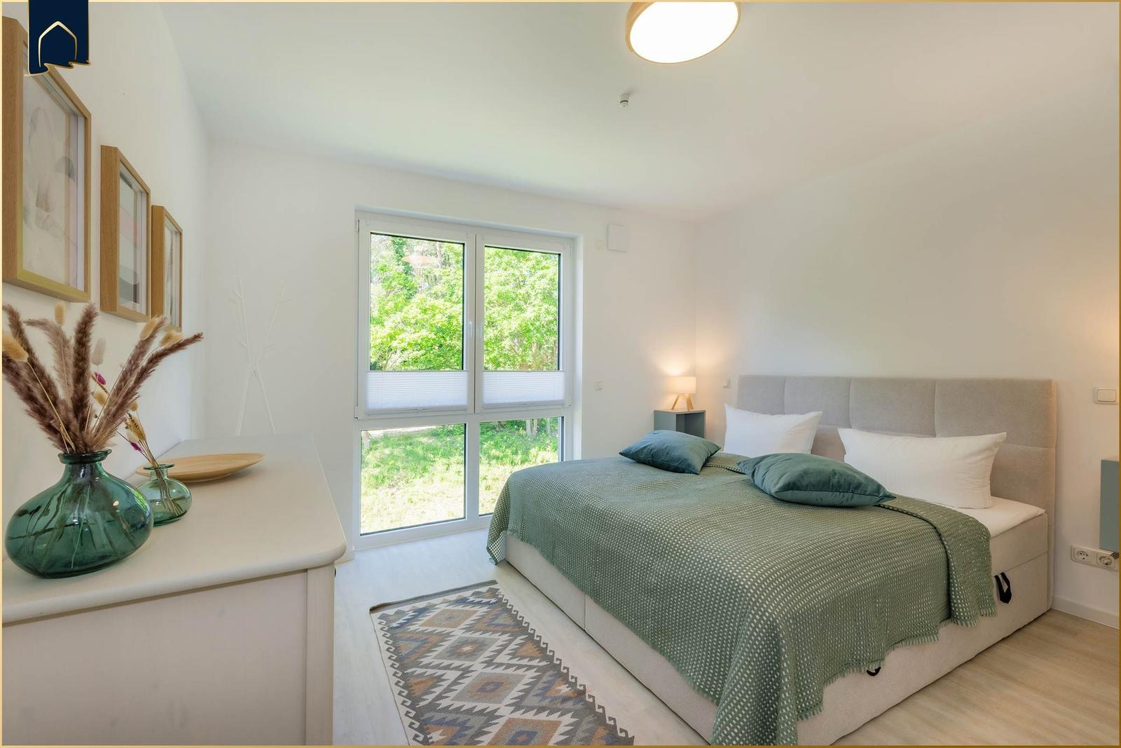 Schlafzimmer mit Bett, Fenster und Schrank. Grün-weiße Bettwäsche und Teppich.