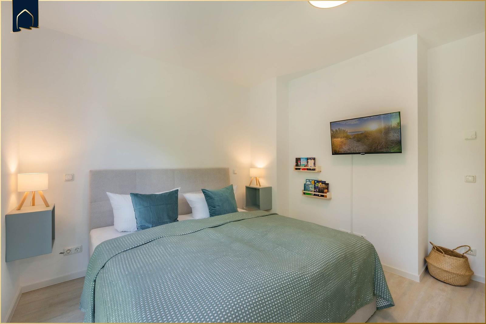 Schlafzimmer mit Bett, Nachttischen und Fernseher an der Wand.