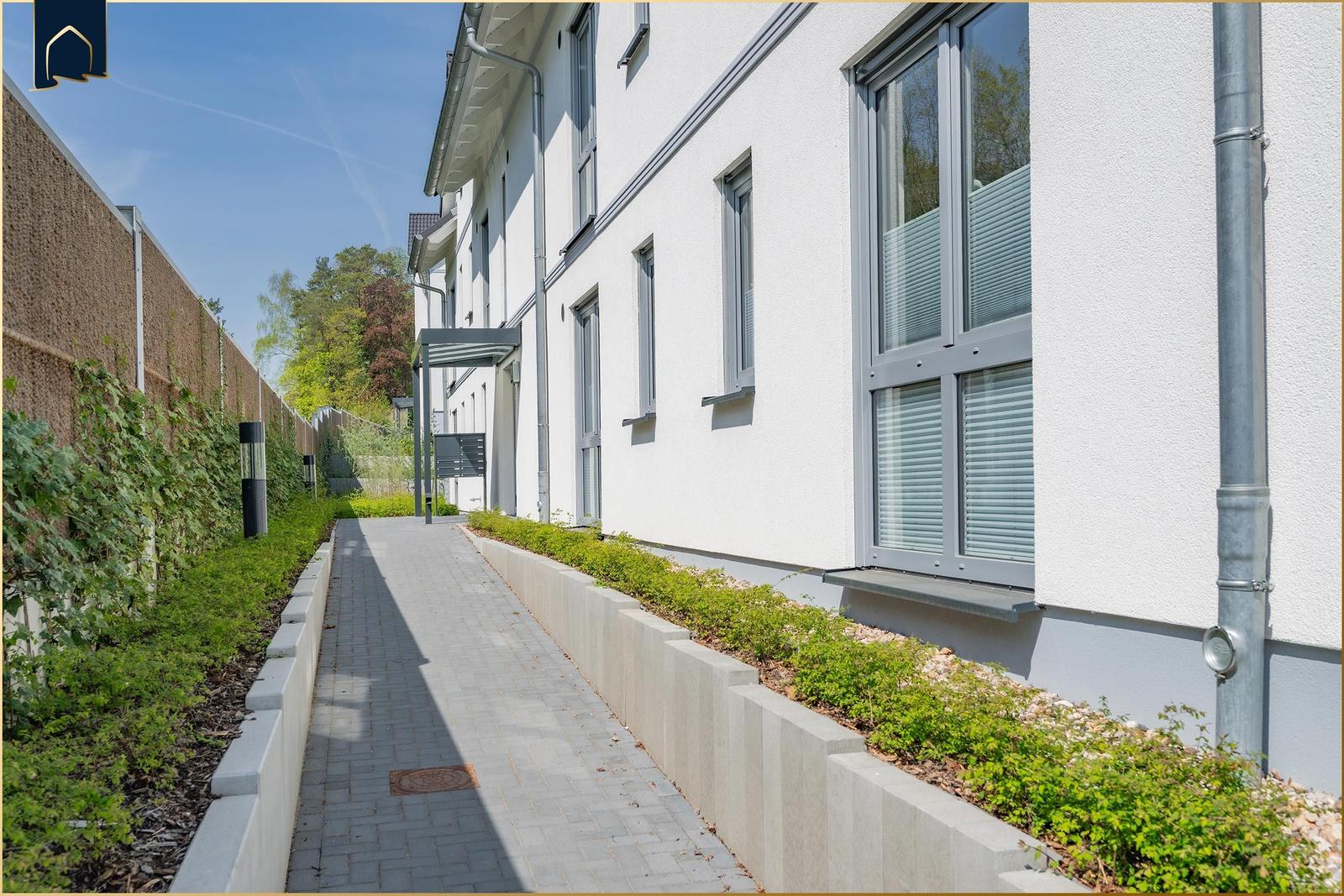 Gehweg neben modernem Haus mit Fenstern und Grünflächen.