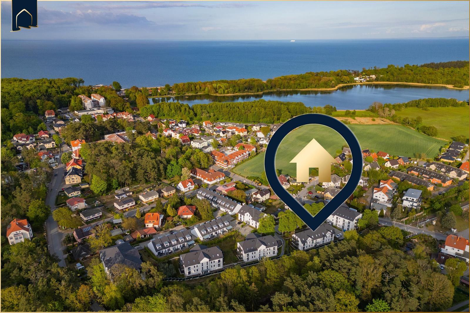 Aerial view of a coastal town with houses, forests, and a lake near the sea.