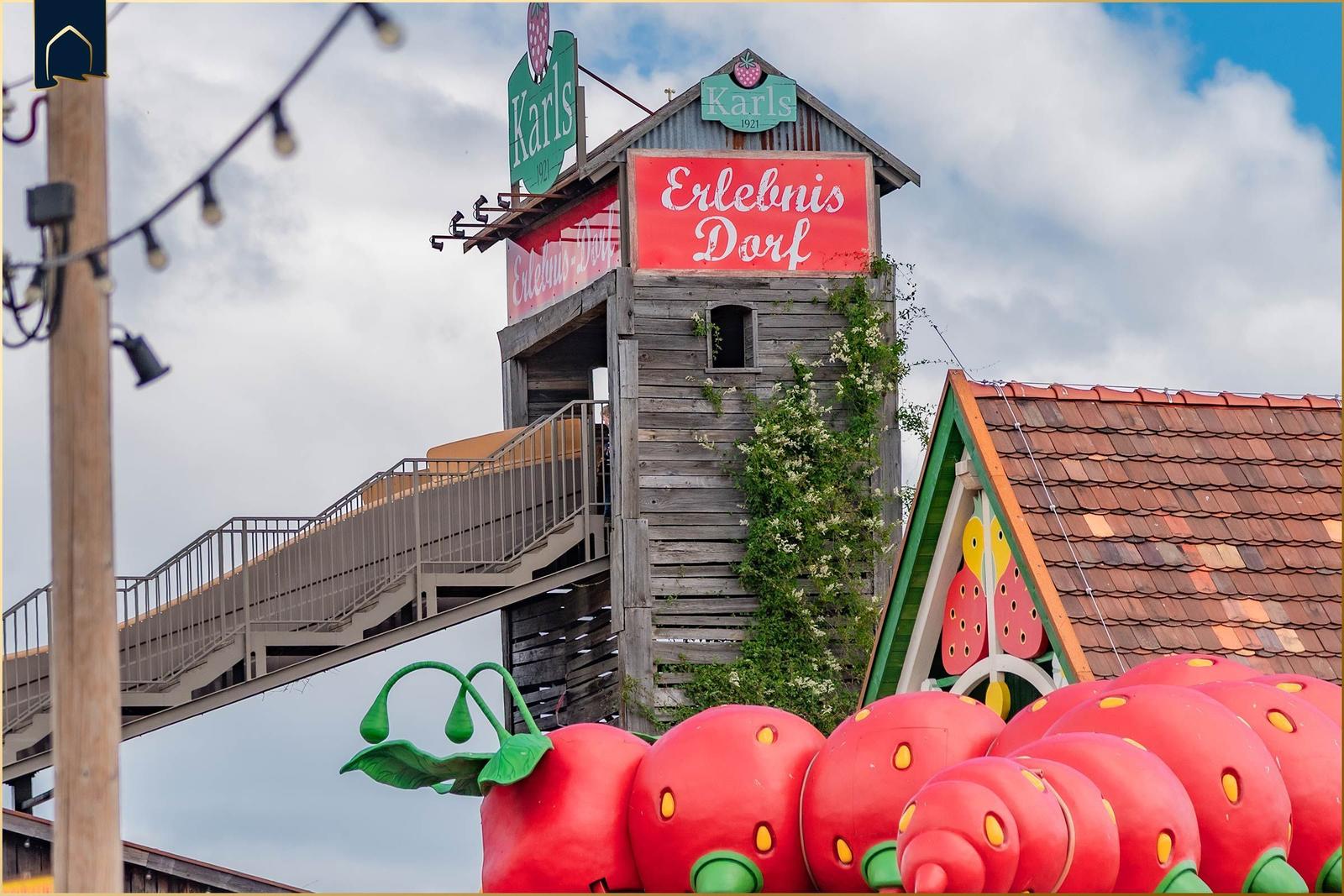 Erlebnis Dorf mit großen Erdbeeren und Holzgebäude unter bewölktem Himmel.