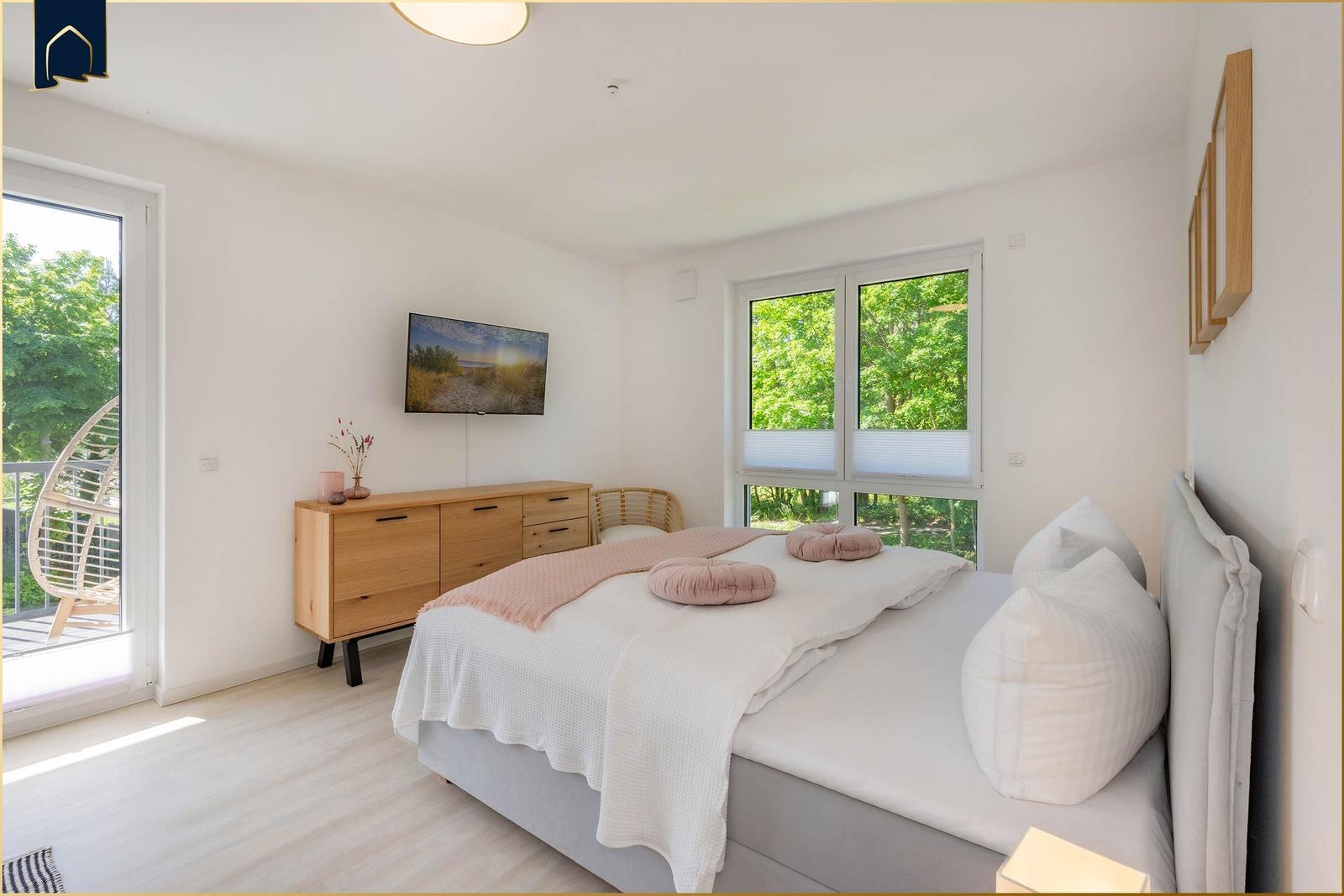 Schlafzimmer mit Bett, Schrank und TV. Fenster mit Blick auf Grün.