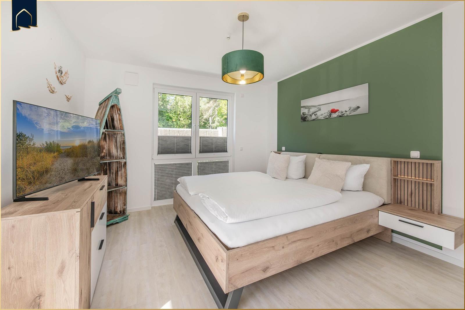 Schlafzimmer mit Bett, Fernseher und Fenster zur Außenseite.