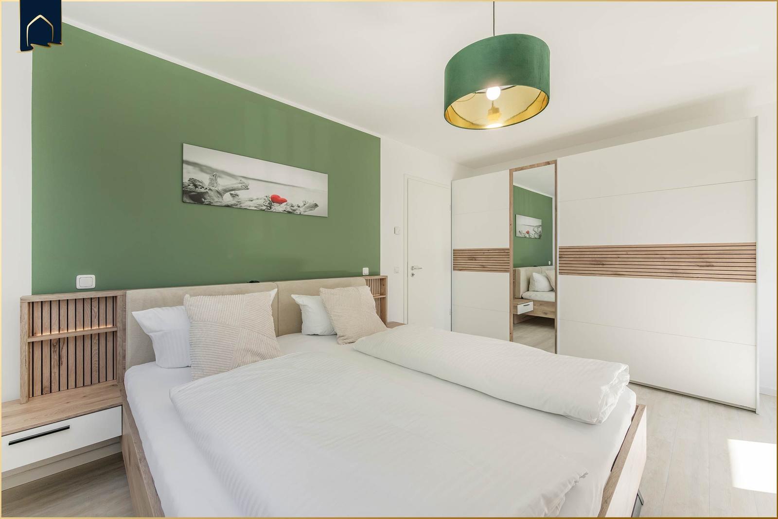 Schlafzimmer mit Bett, grüner Wand und großer Lampe.