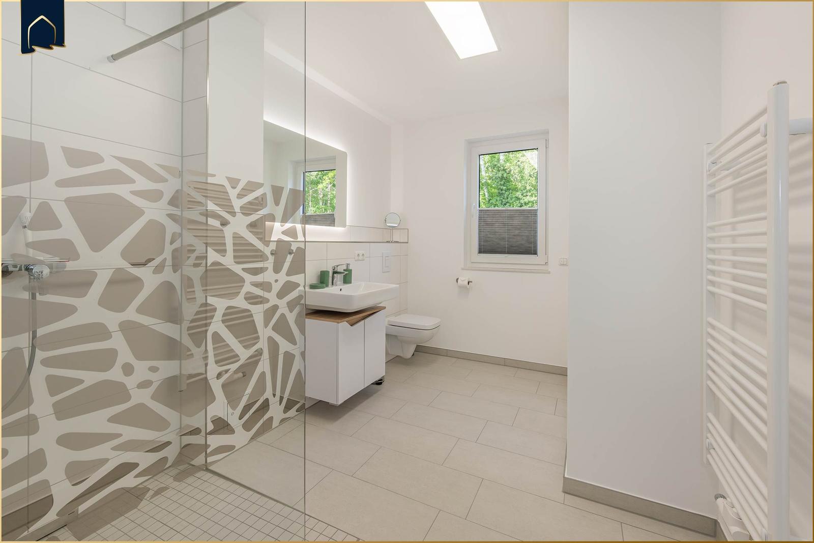 Badezimmer mit Dusche, Waschbecken und Toilette. Fenster mit Blick auf Grün.