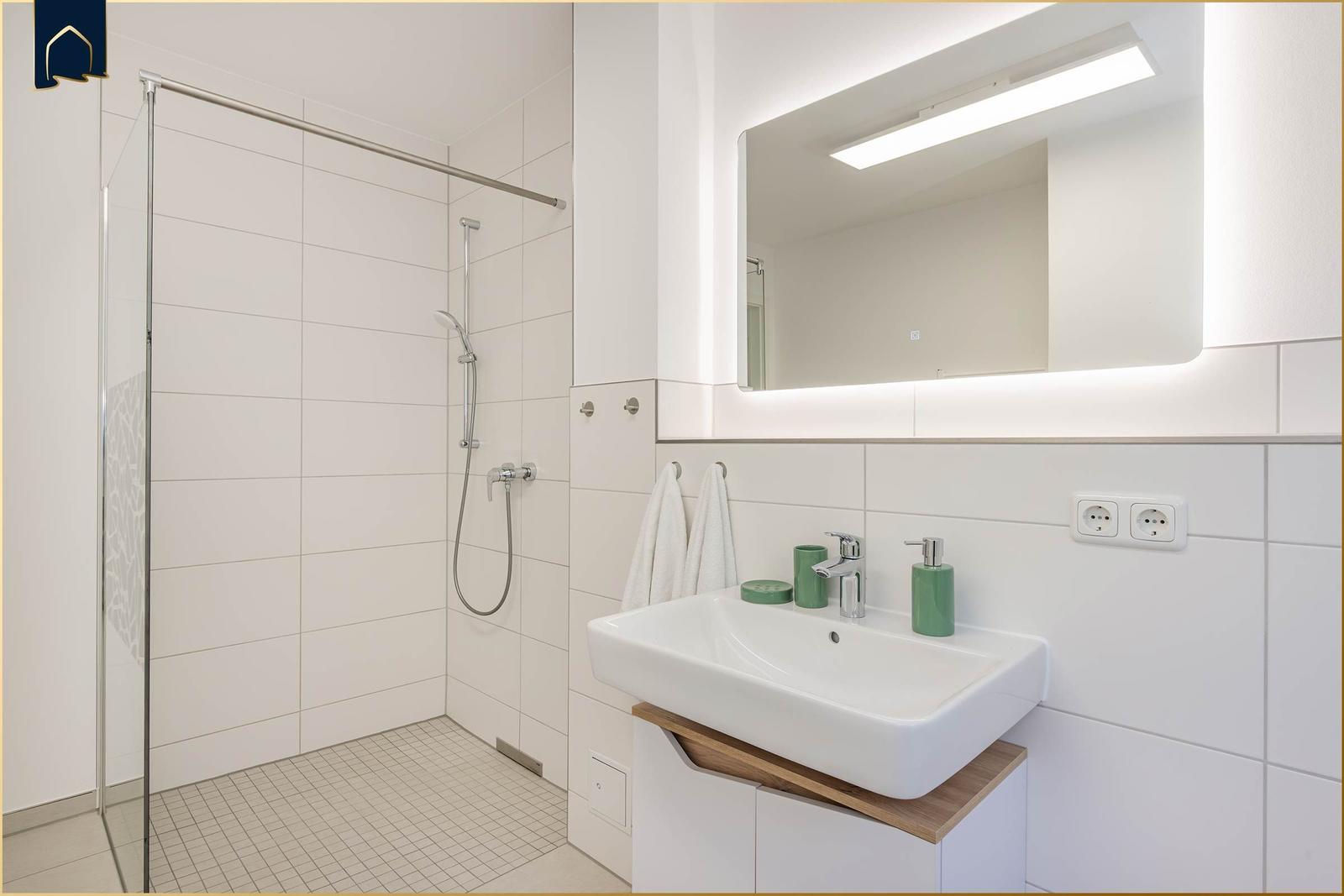 Bad mit Dusche, Waschbecken und beleuchtetem Spiegel