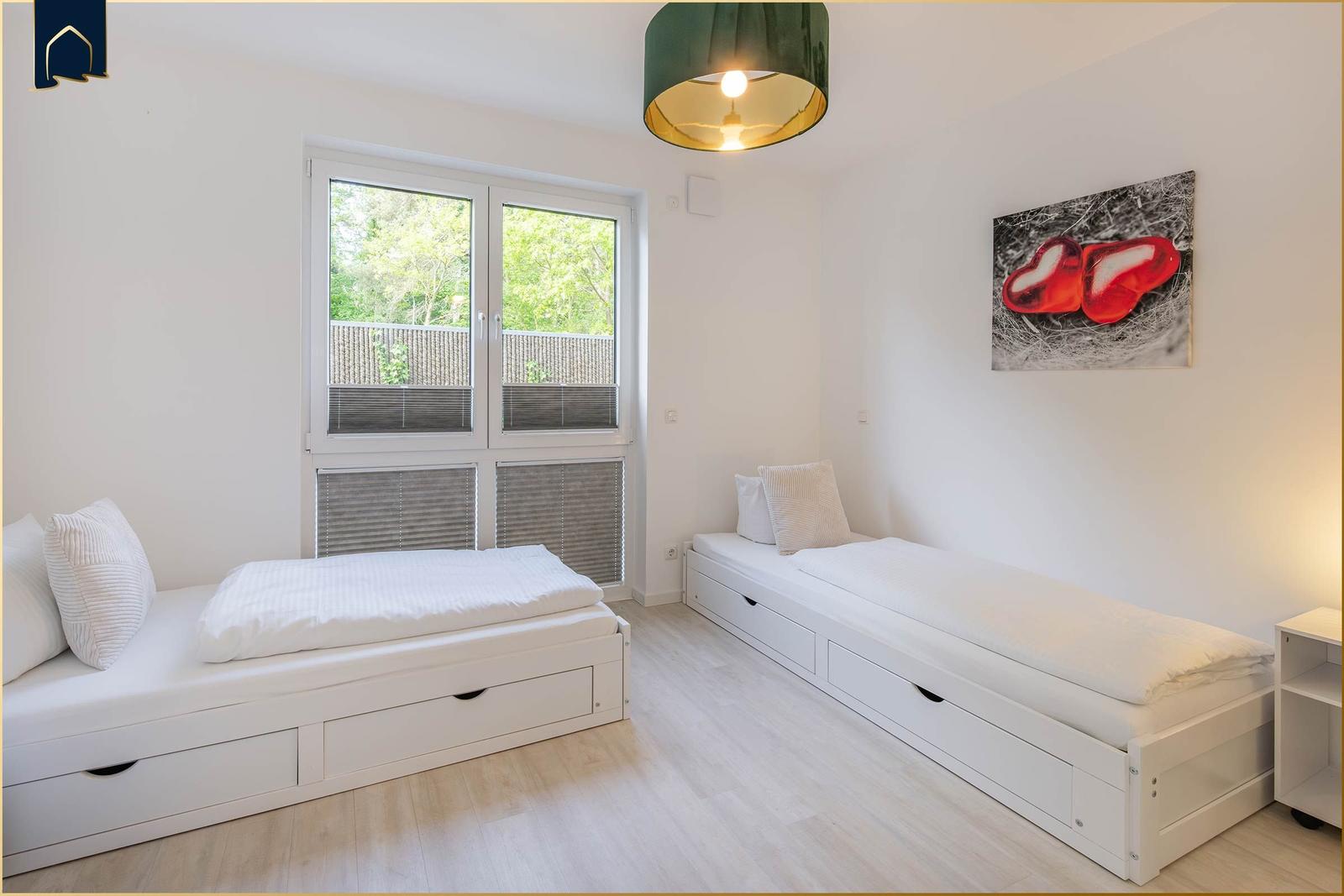 Zwei weiße Schlafstellen mit Schubladen, Fenster und Wandbild.