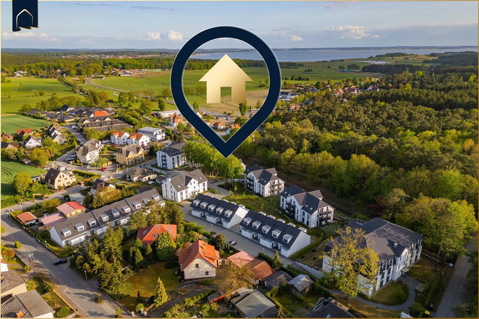 Luftbild von Wohnhäusern mit Wald und See im Hintergrund.