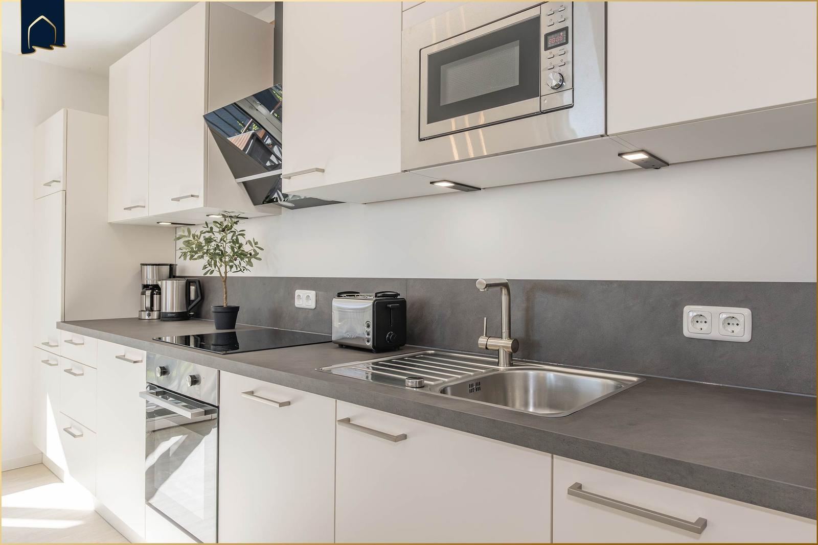 Moderne Küche mit Edelstahlspüle, Dunstabzugshaube und integriertem Mikrowellenherd.