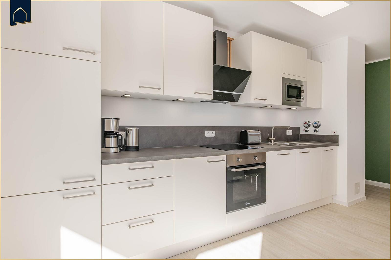 Moderne Küche mit weißen Schränken, Edelstahlgeräten und grauer Arbeitsplatte.