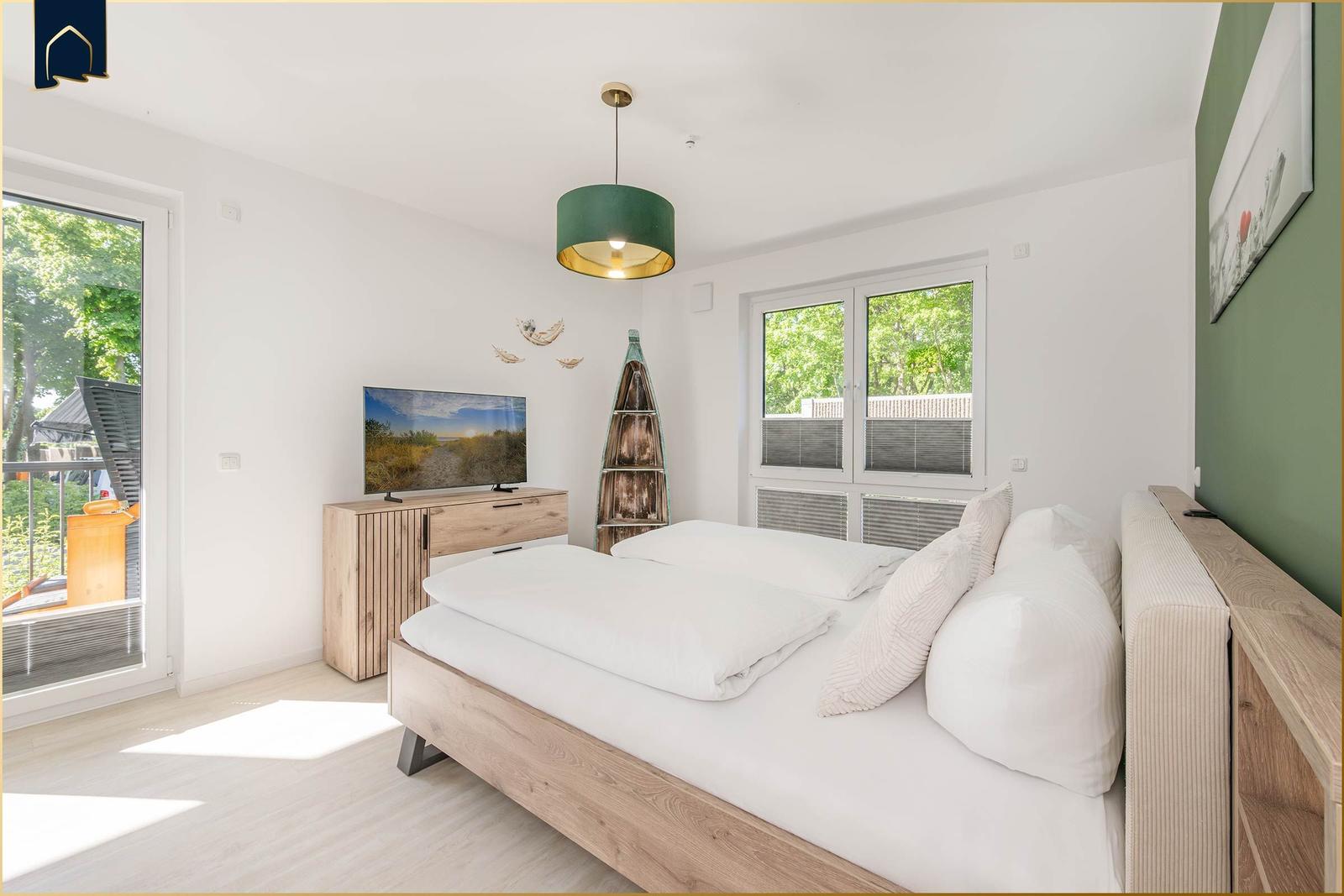 Schlafzimmer mit Bett, Fernseher und Fenster zur Terrasse.