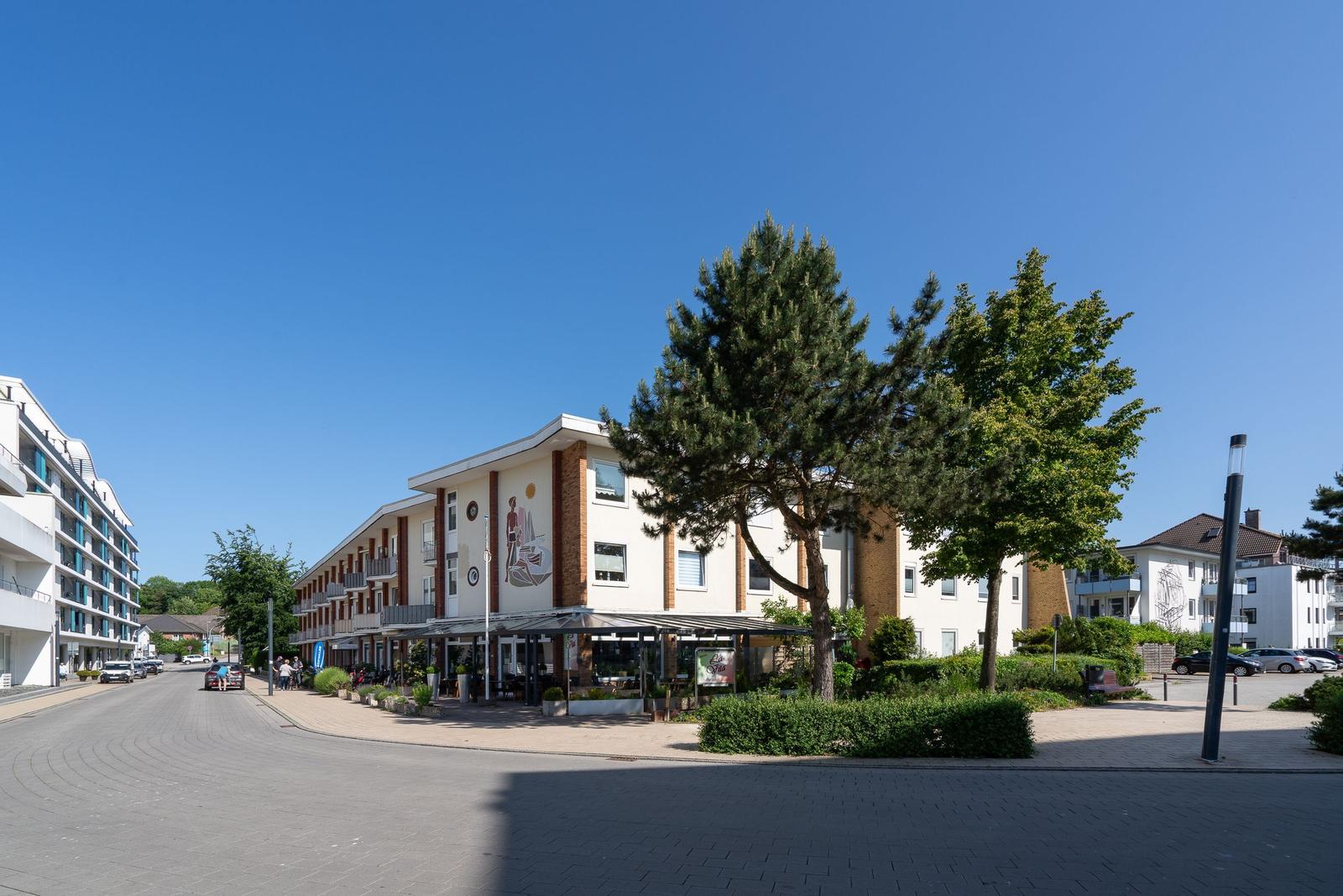 Ferienhaus mit Terrasse und Bäumen an sonnigem Tag.