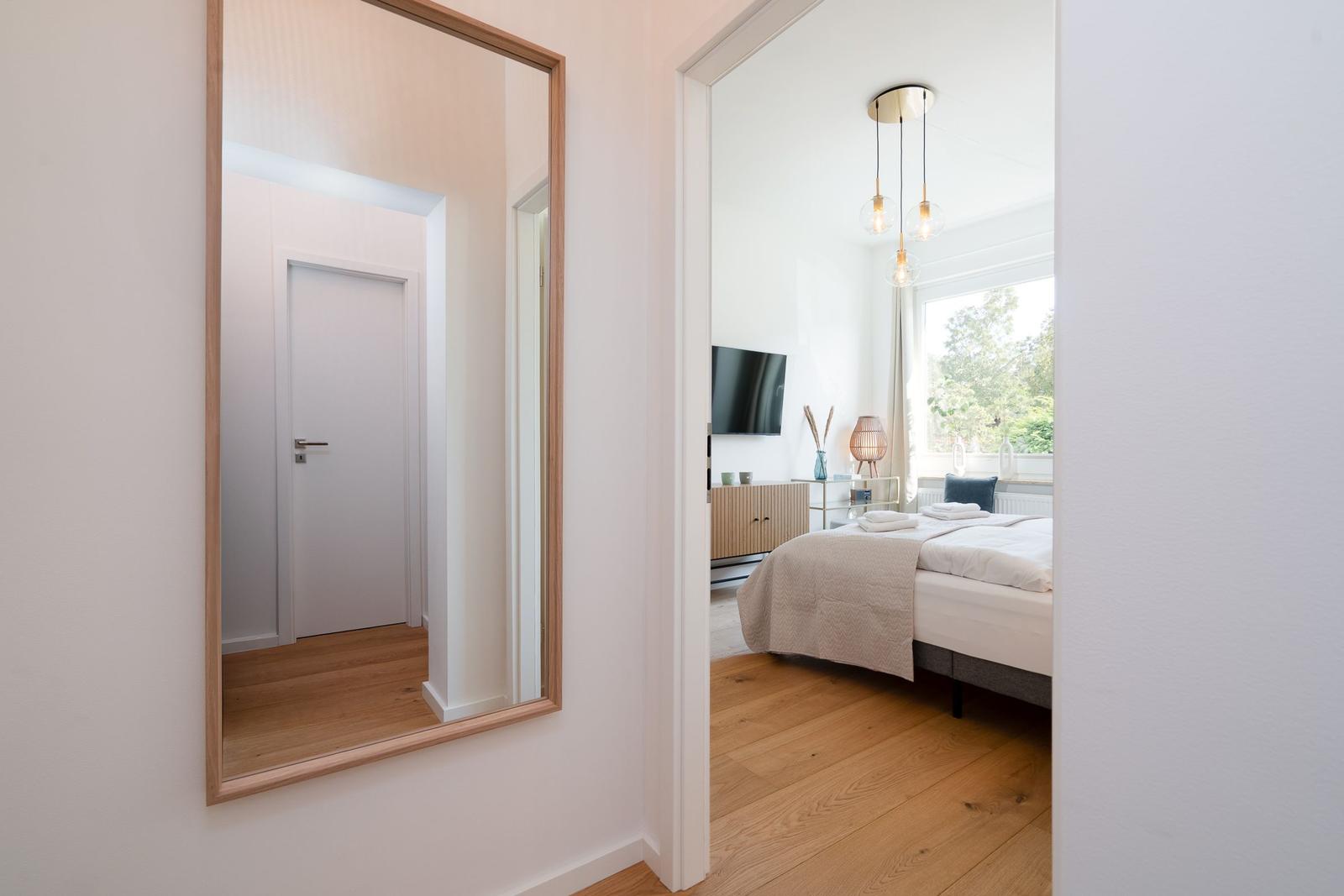 Schlafzimmer mit Bett, Fernseher und Fenster. Spiegel an der Wand.