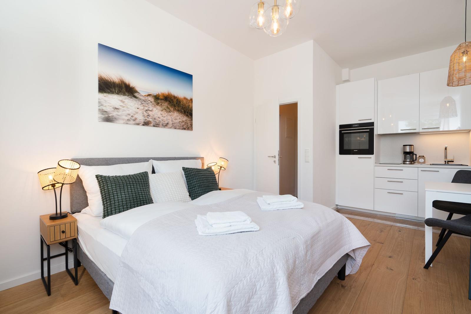 Schlafzimmer mit Bett, Nachttisch und Küchenbereich.