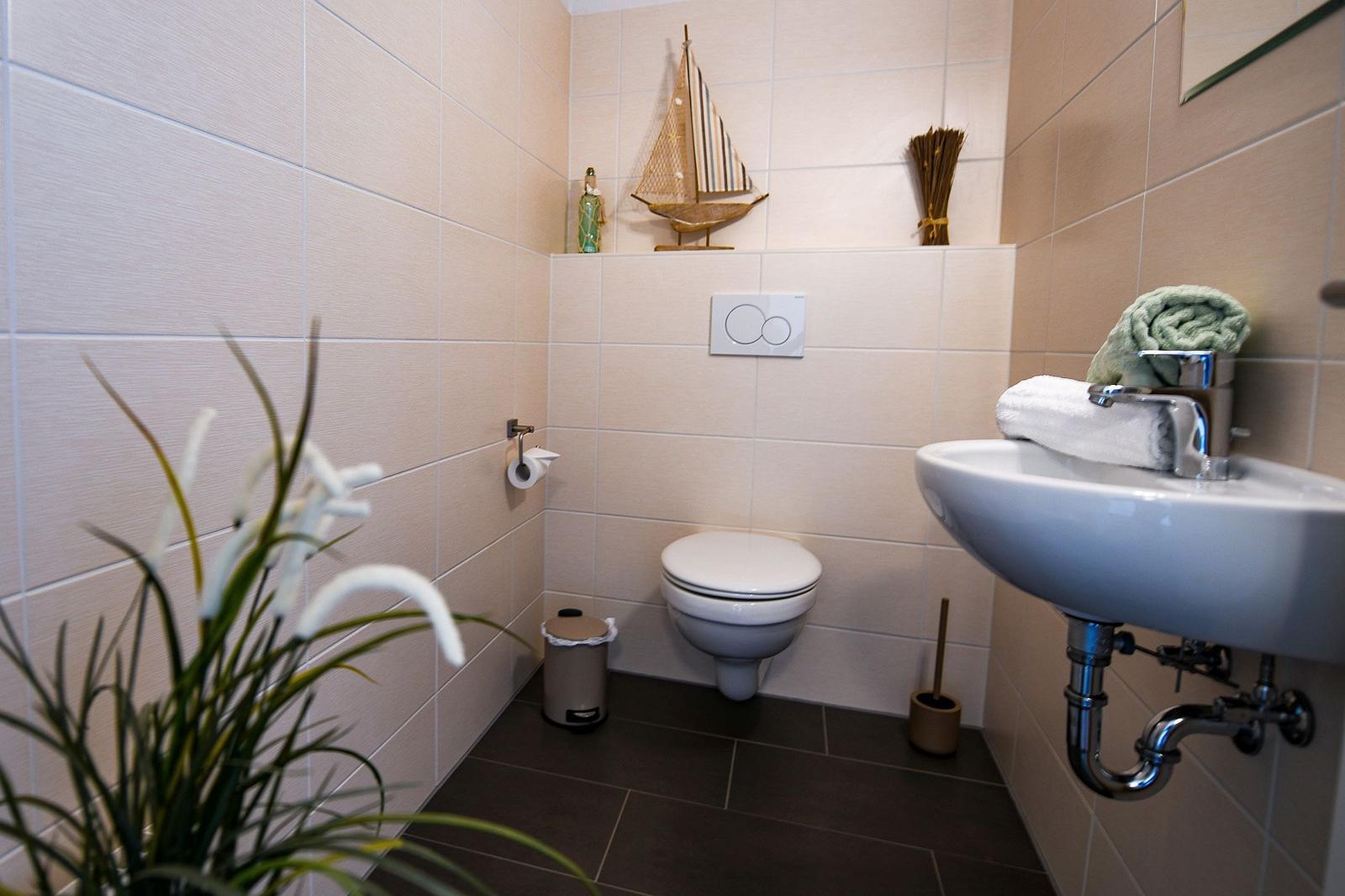 Badezimmer mit Toilette, Waschbecken und Pflanze. Dekoration mit Segelboot.