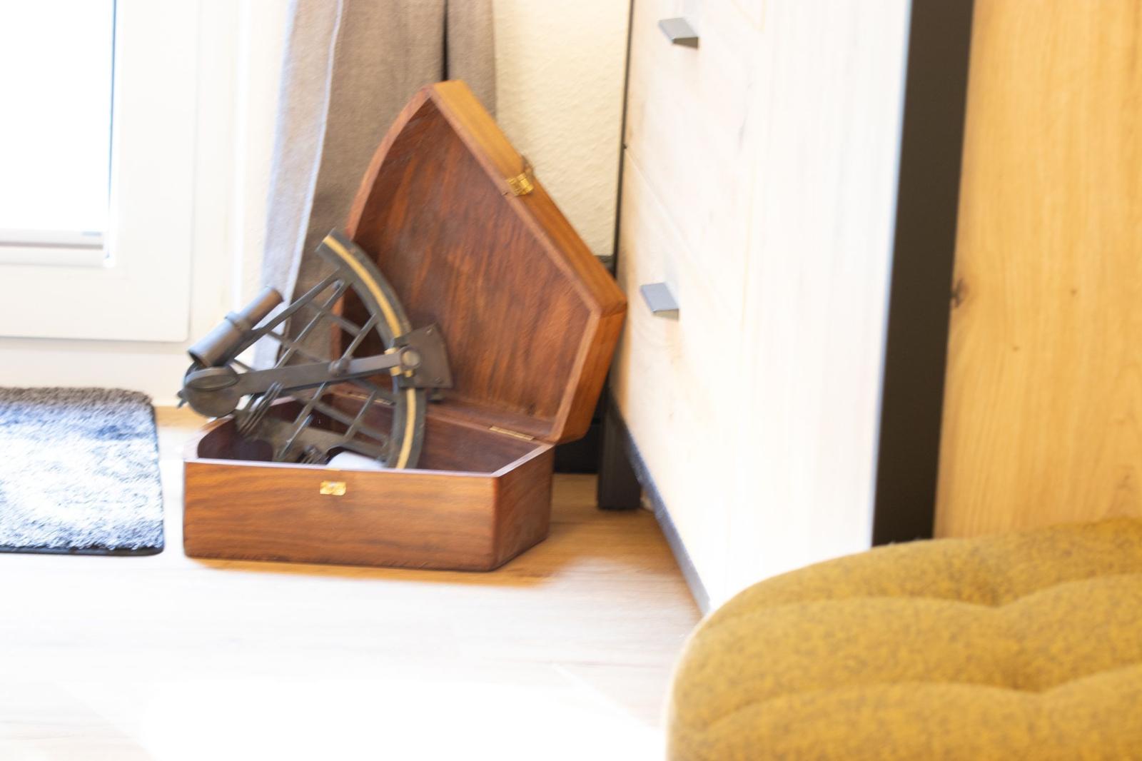 Holzkiste mit Astrolabium steht im Raum neben Schrank und Fenster.
