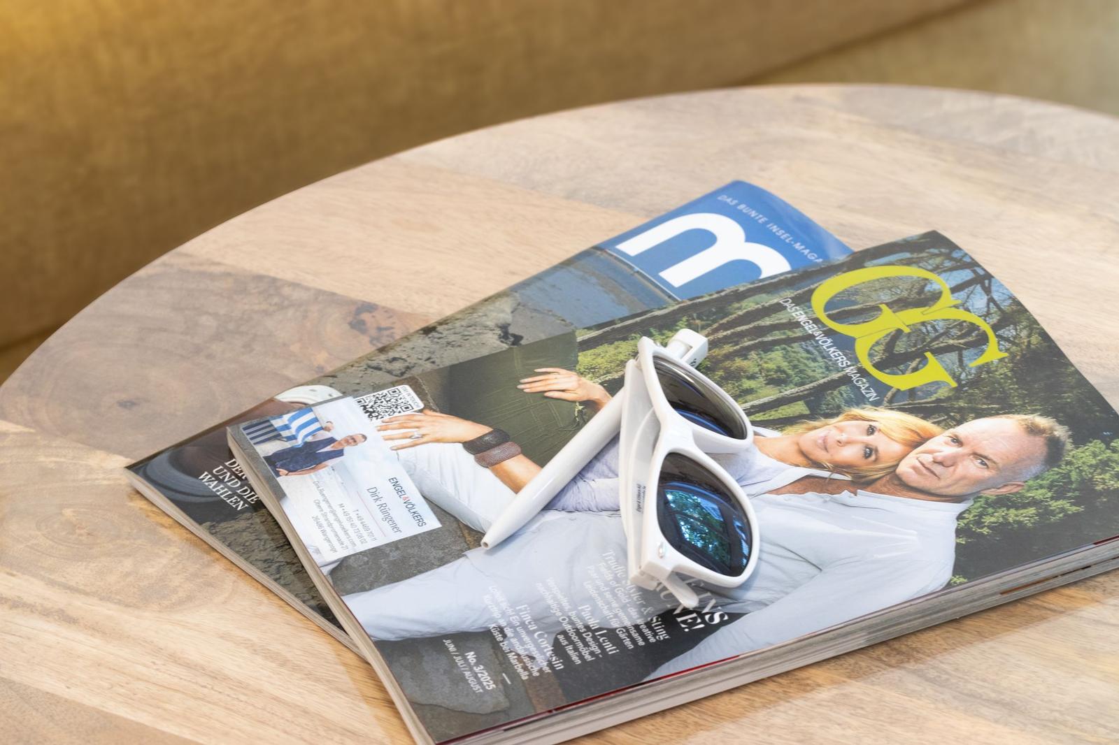 Auf einem runden Tisch liegen Zeitschriften und weiße Sonnenbrille.