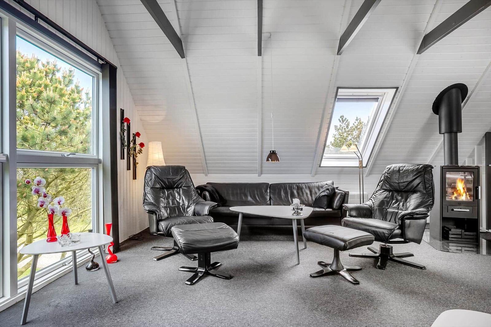 Wohnzimmer mit schwarzen Ledermöbeln, Kamin und großen Fenstern.