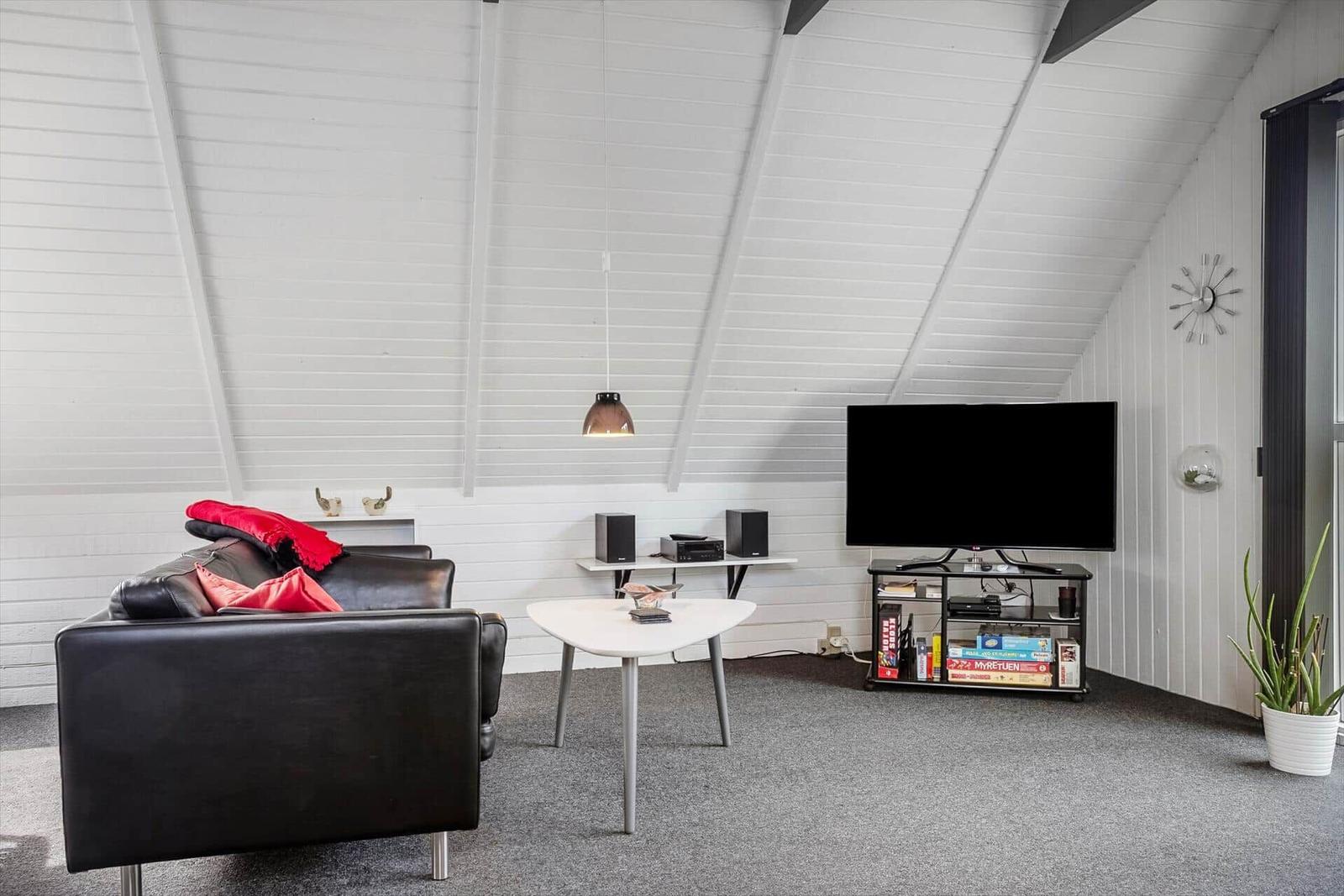 Wohnzimmer mit Sofa, Fernseher und Tisch unter schrägem Dach