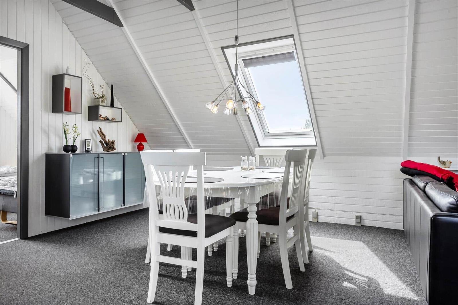 Essbereich mit weißem Tisch und Stühlen unter Dachschrägen mit Fenster.