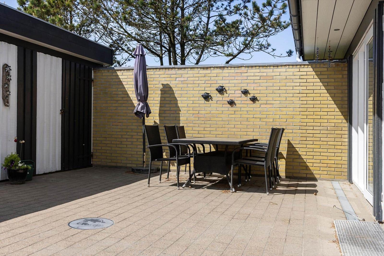 Terrasse mit Tisch, Stühlen und Sonnenschirm vor gelbem Backsteinzaun.