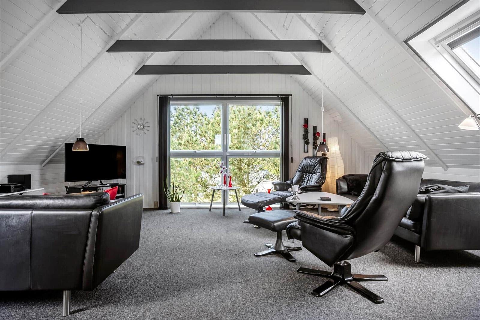 Wohnraum mit schwarzen Ledermöbeln, großem Fenster und schrägen Dachschrägen.