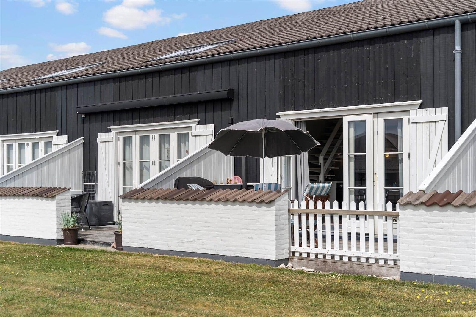 Schwarzes Holzhaus mit weißem Balkon und Gartenbereich unter Sonnenschirm.