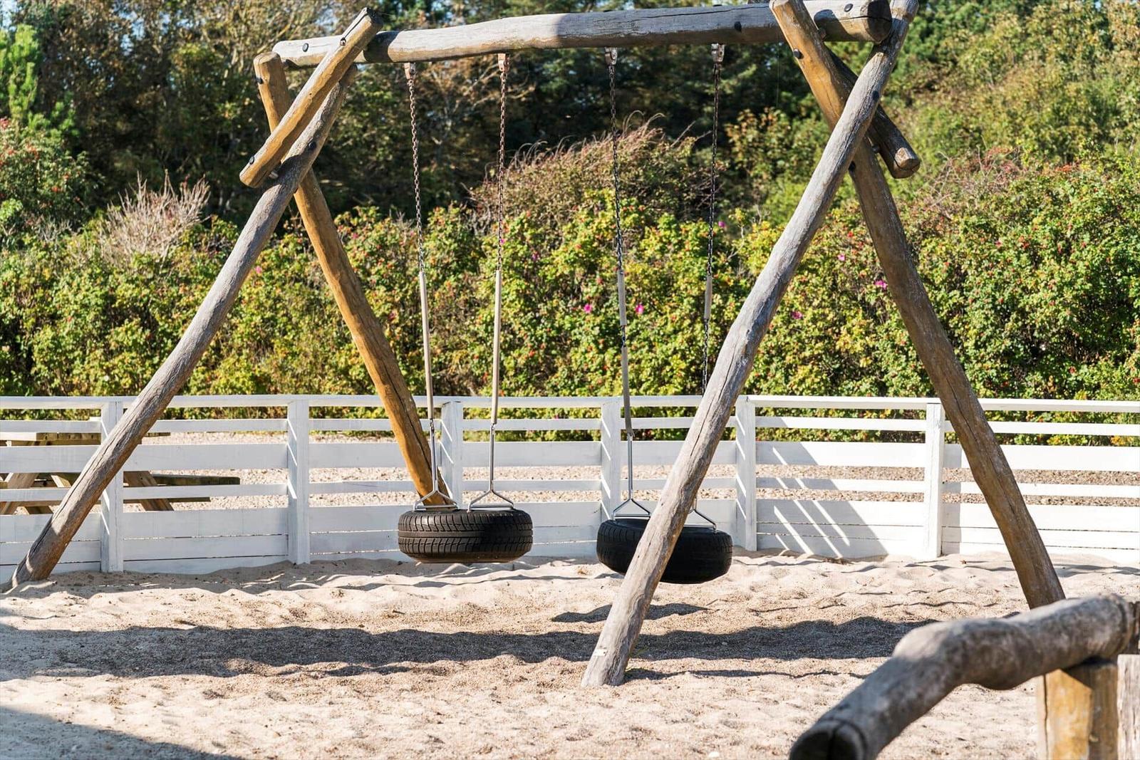 Zwei Reifen-Schaukeln an einem Holzgestell im Sand
