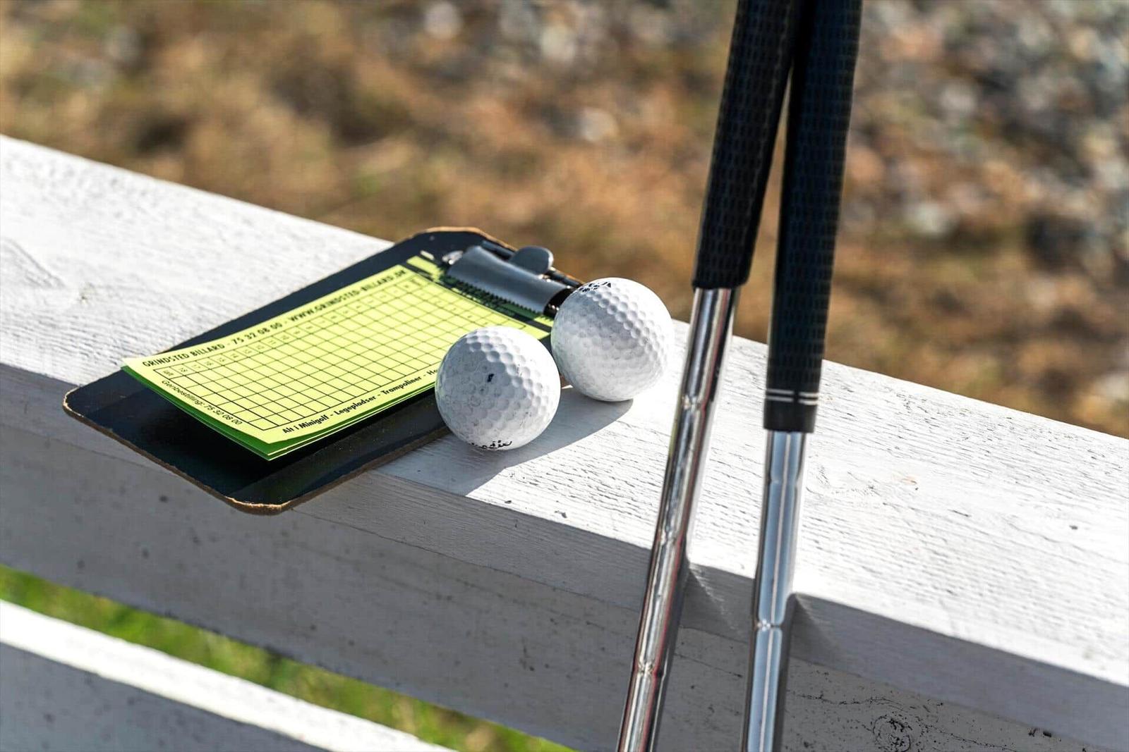 Golfclubs, zwei Bälle und ein Scorecardhalter auf einer weißen Brüstung.