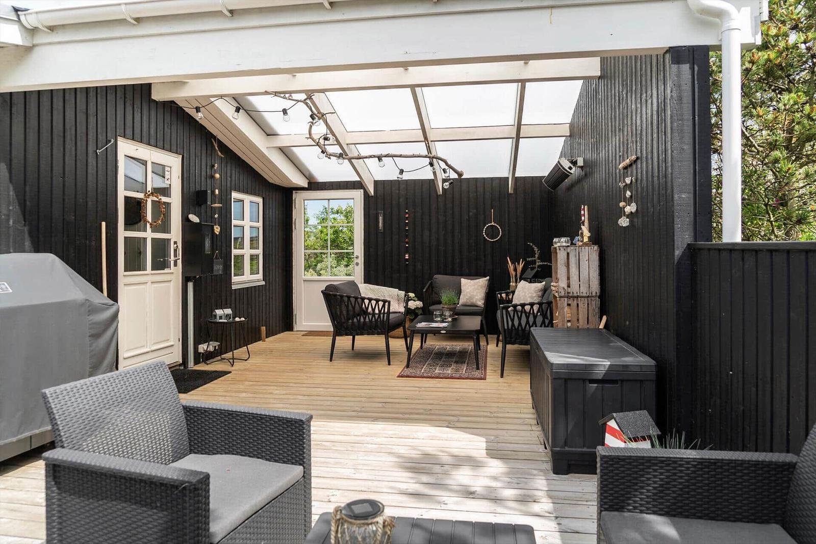 Terrasse mit Sitzgruppe, Grill und Holzboden unter Glasdach.
