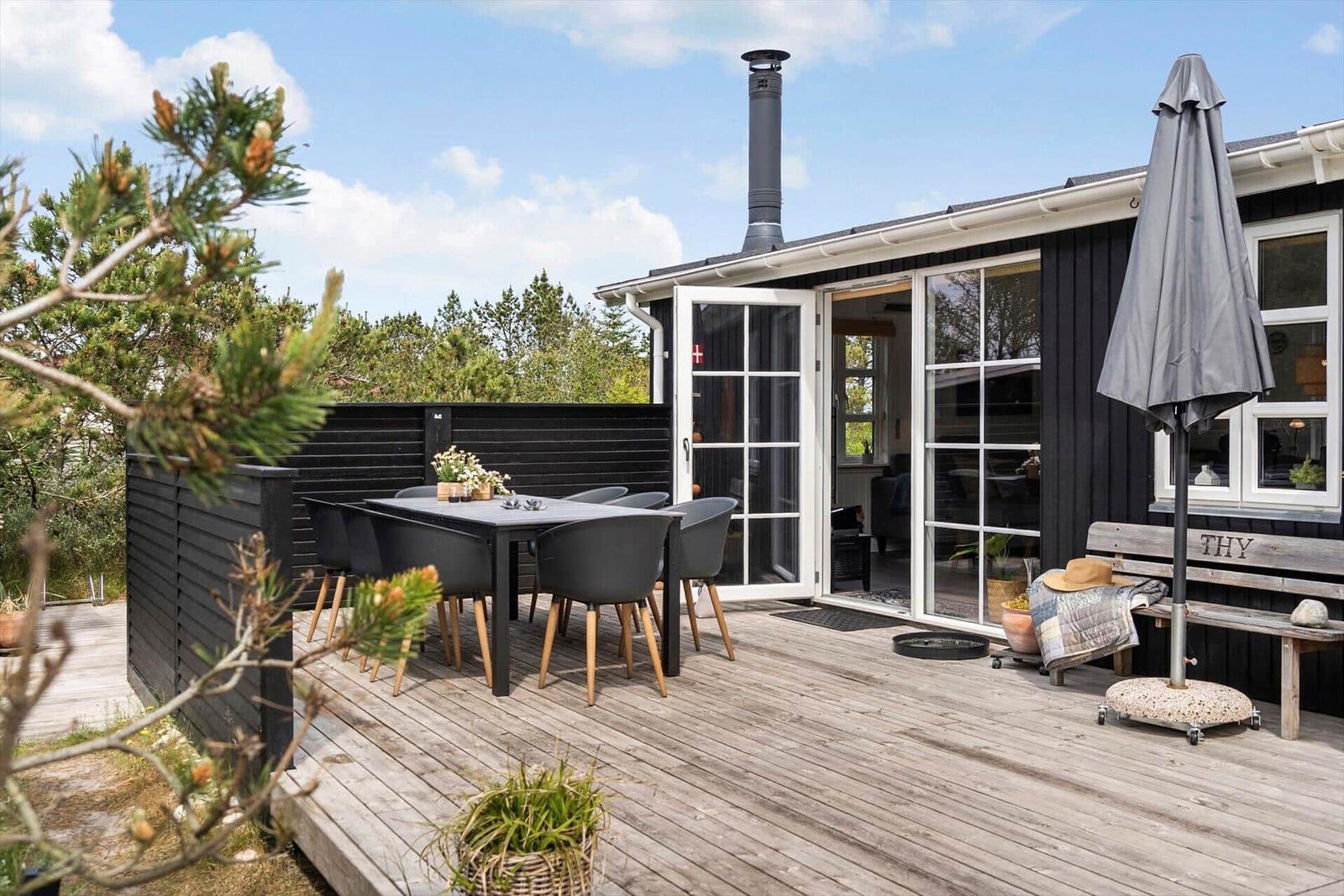 Terrasse mit Tisch, Stühlen und Schirm vor einem Haus mit Glasfront.
