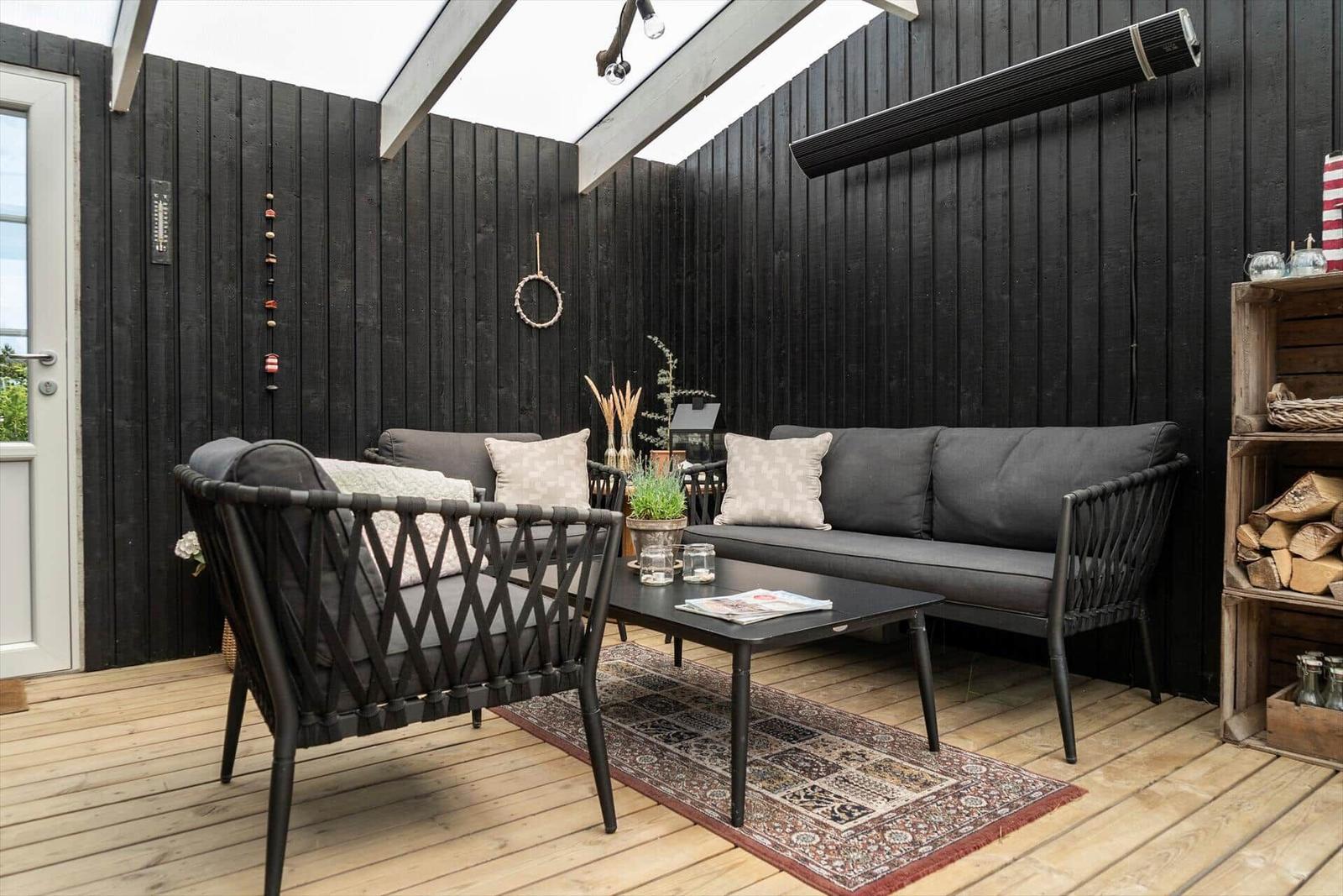 Terrasse mit Sofa, Sitzgelegenheit und Holzboden. Schwarze Wände und Holzrahmen.