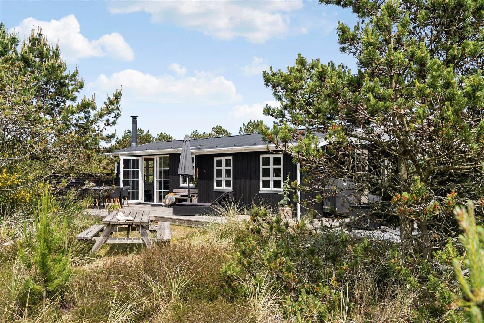 Schwarzes Haus mit Terrasse, Grill und Picknicktisch unter Bäumen.