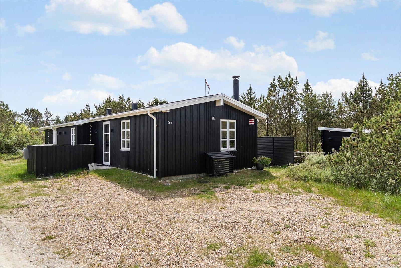 Schwarzes Holzhaus mit weißen Fenstern und Dach, umgeben von Bäumen und Gras.