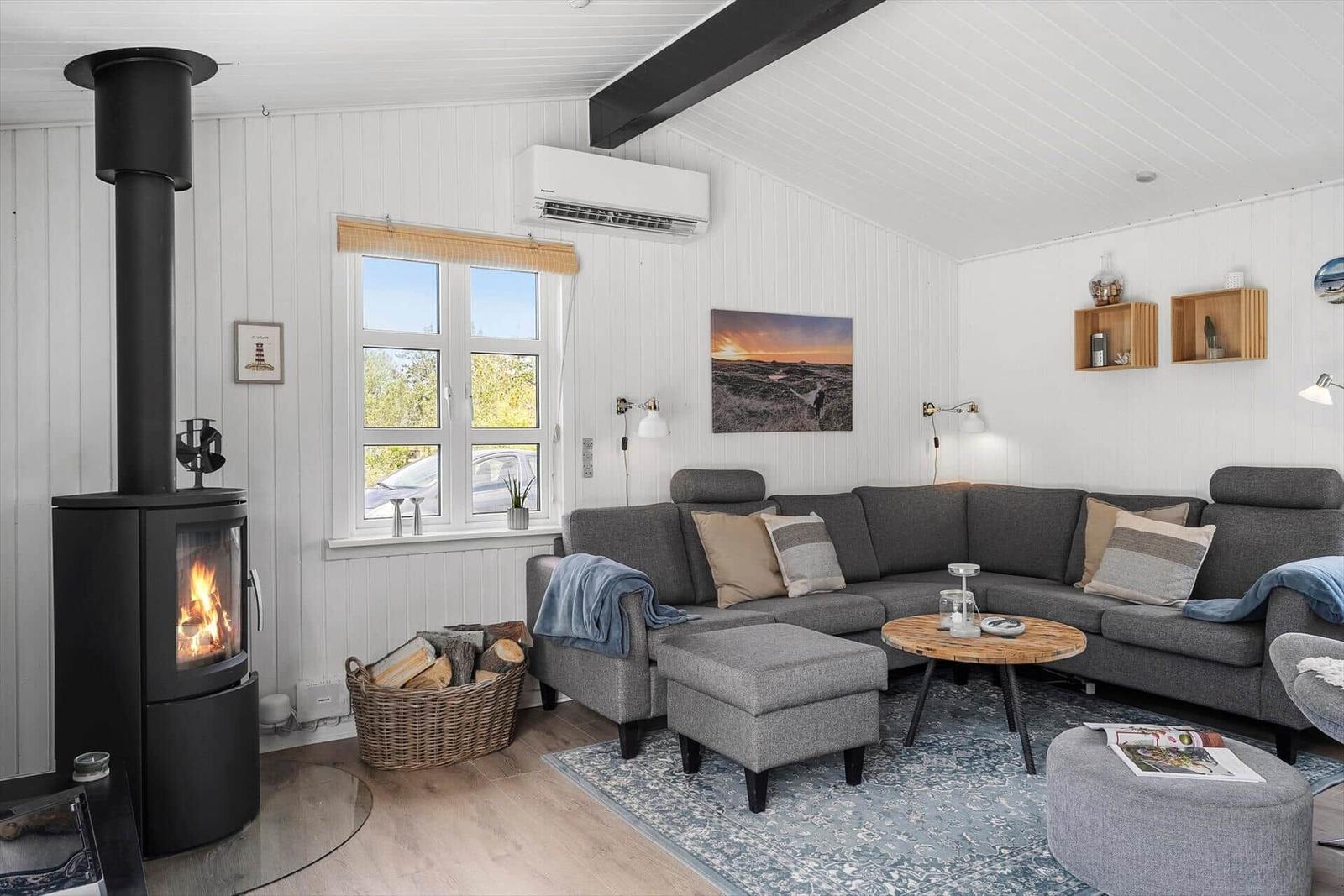 Wohnzimmer mit Kamin, Sofa und Fenster. Holzdielen und weiße Wände.