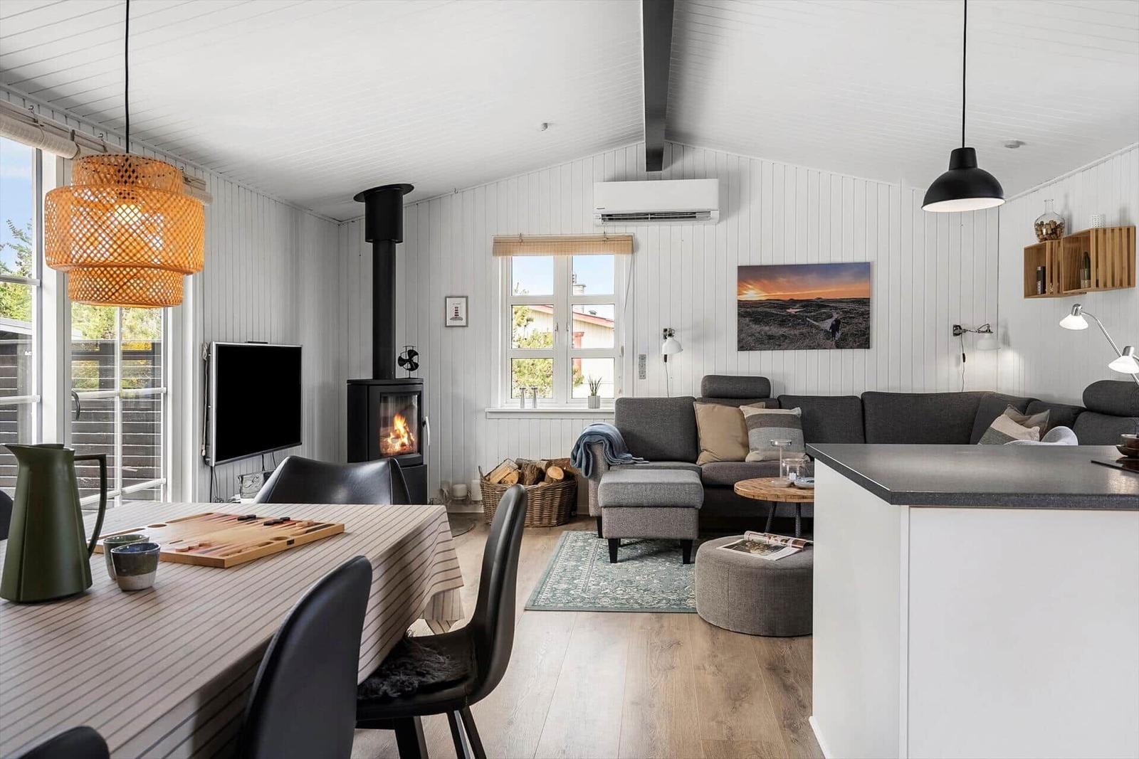 Wohnbereich mit Sofa, Kamin und Esstisch. Weiße Wände und Holzboden.