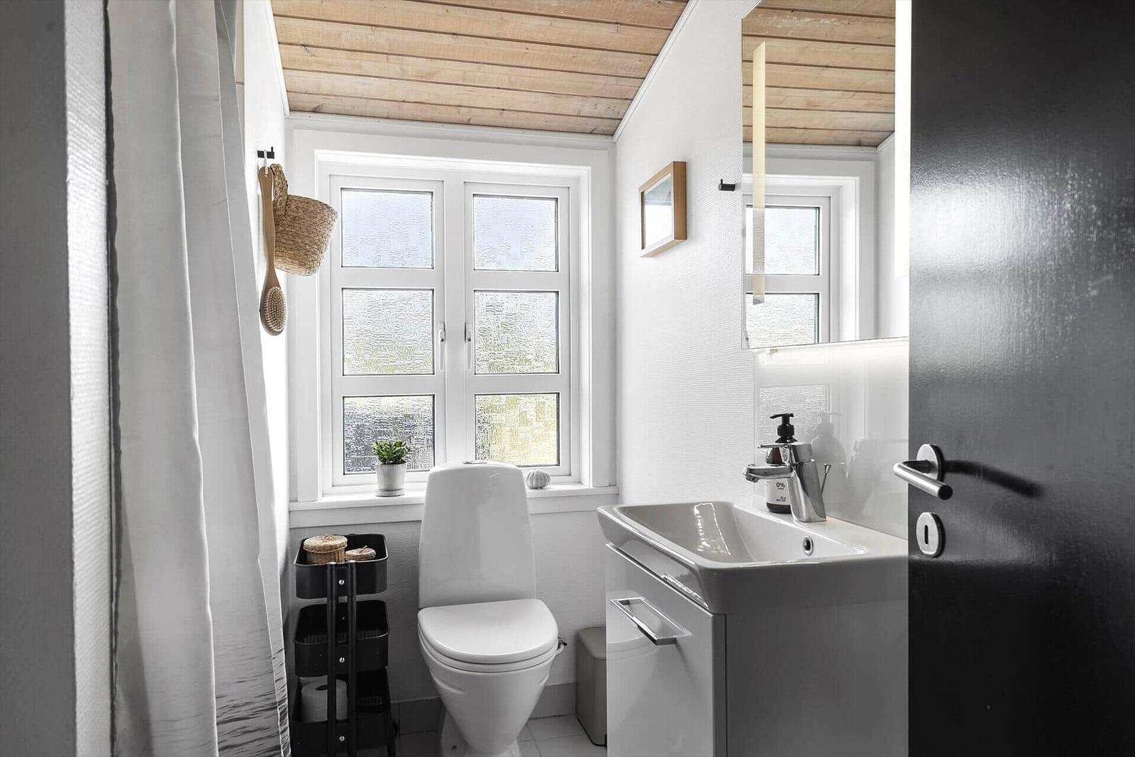 Badezimmer mit Toilette, Waschbecken und Fenster. Holzdecke und weiße Wände.