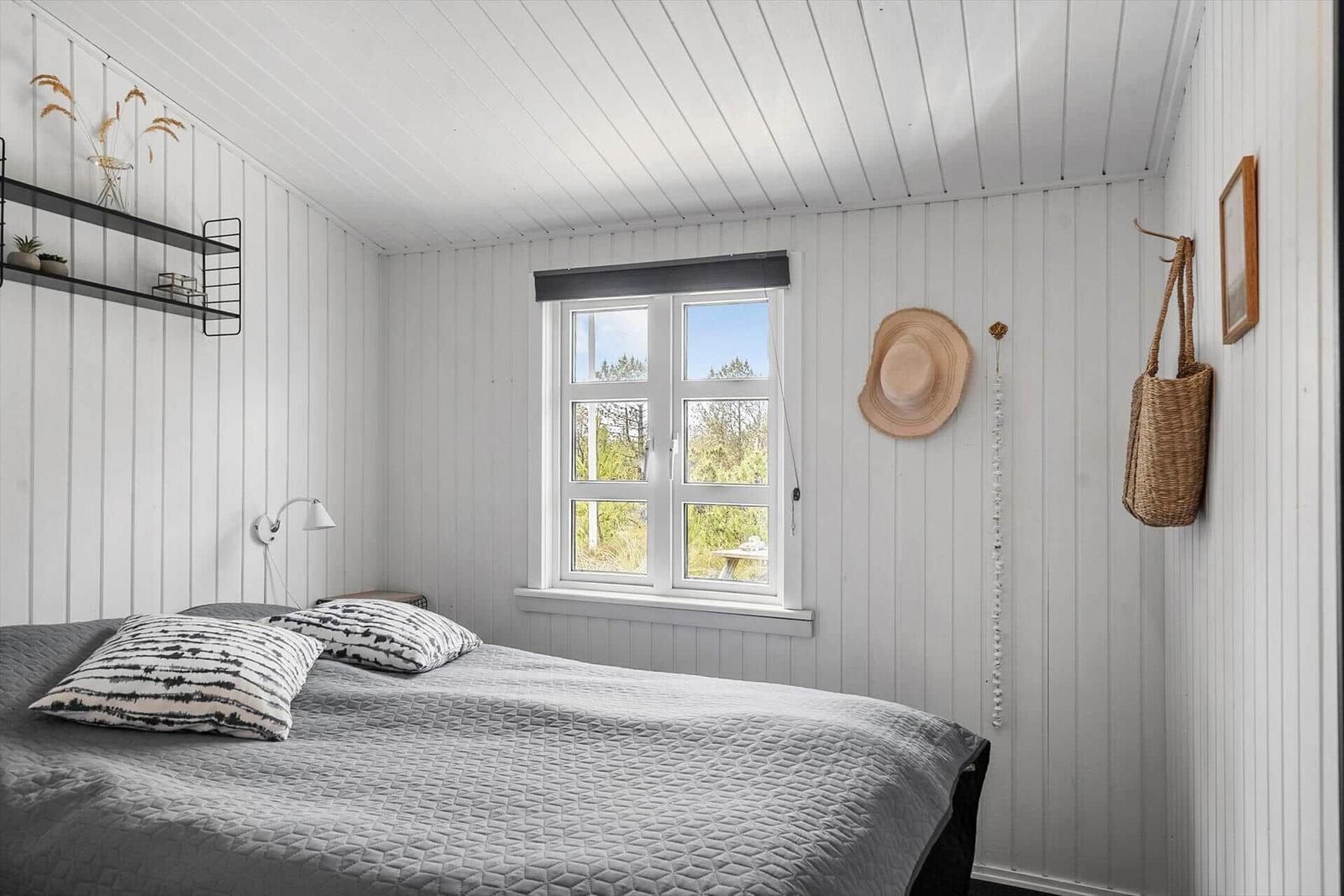Schlafzimmer mit Bett, Fenster und Wandregal.