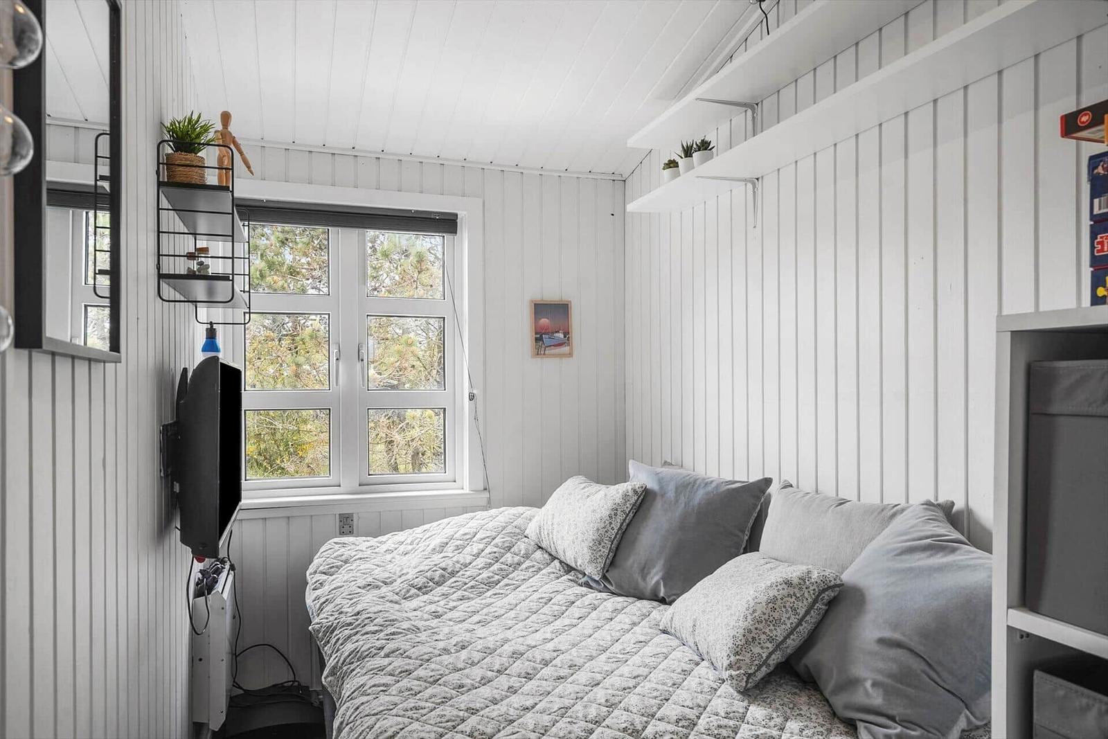 Schlafzimmer mit Bett, Fenster und Wandregalen.
